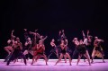 Dancers on stage mid-performance with purple down lights and abstract costumes.